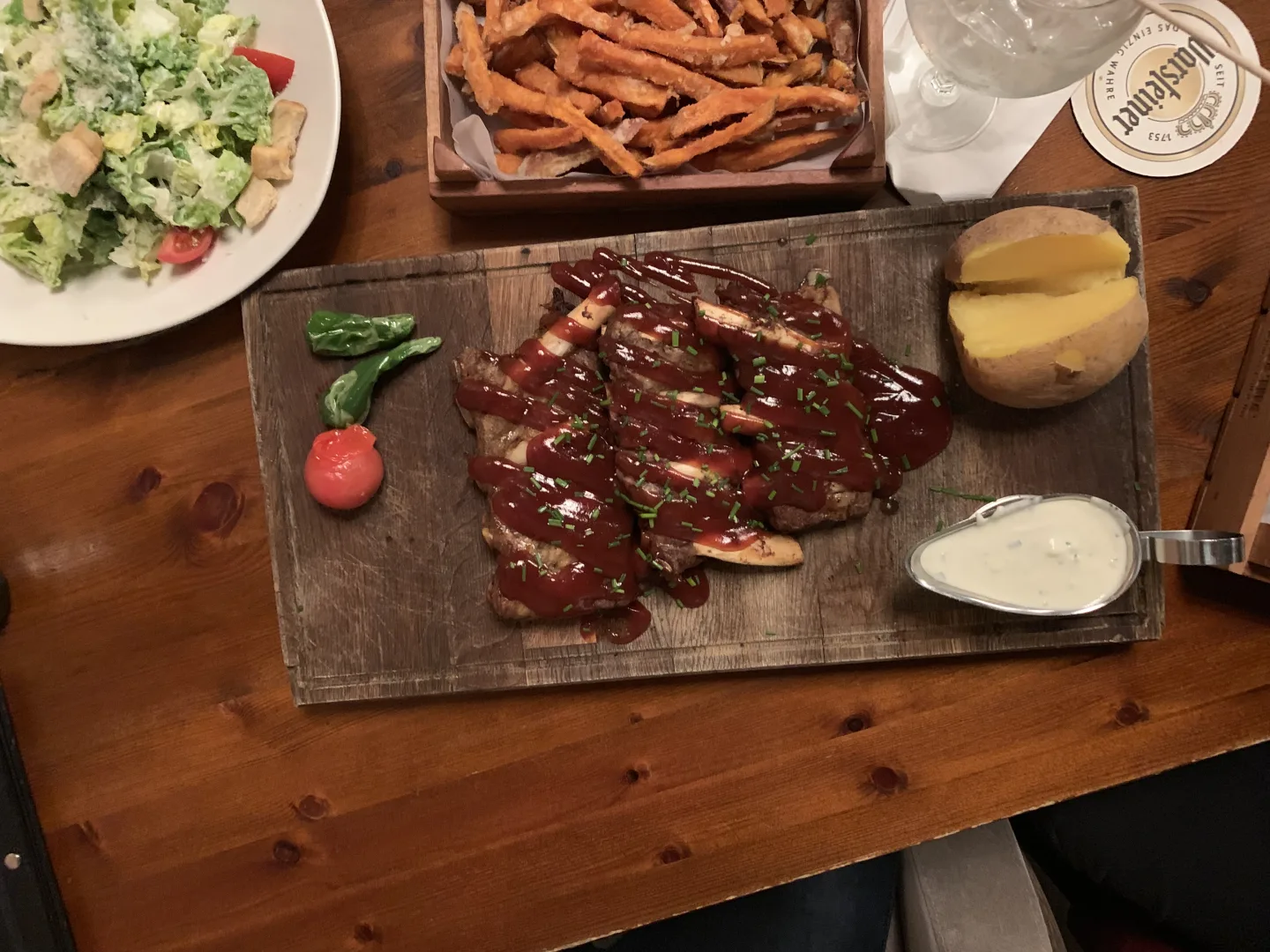 Steak auf Holzbrett mit BBQ-Sauce Suesskartoffelpommes und Caesar Salad