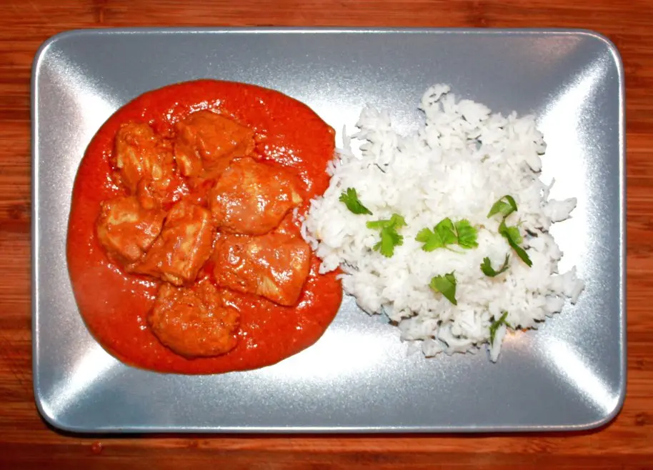Chicken Tikka Masala fertig auf dem Teller mit Sauce und Beilagen