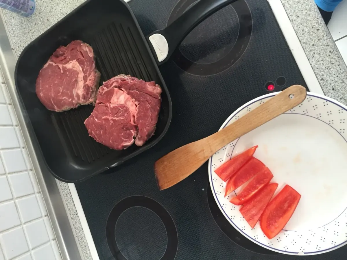Zwei rohe Ribeye-Steaks auf einer schwarzen Grillpfanne mit Paprika auf separatem Teller