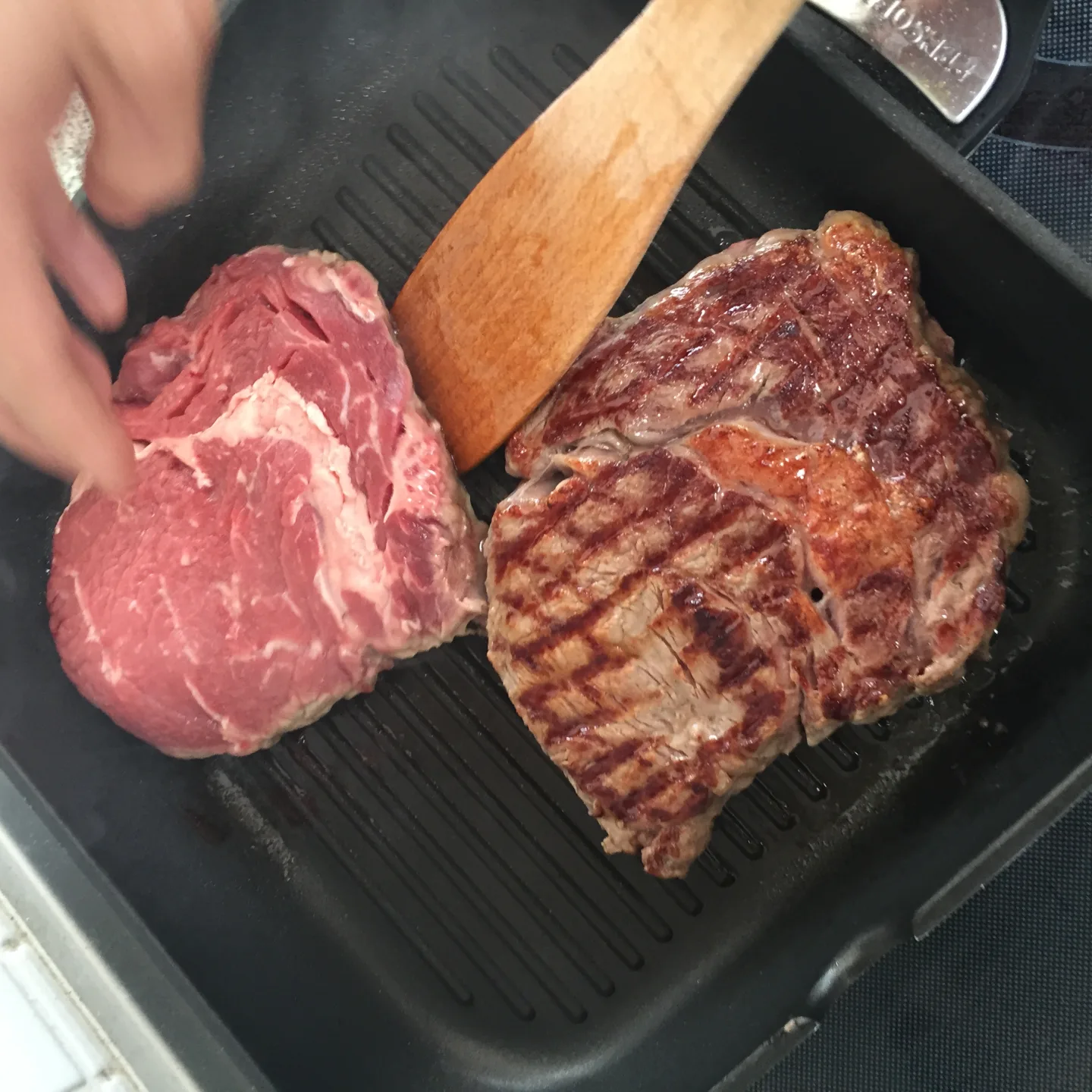 Zwei Steaks auf Grillpfanne eines roh und eines mit perfekten Grillstreifen