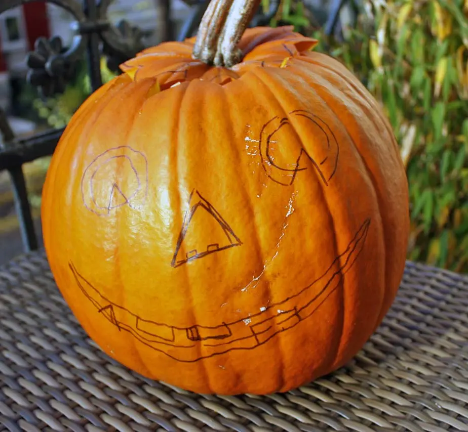 Halloween-Kürbis mit aufgezeichnetem Gesicht als Skizze vor dem Ausstechen