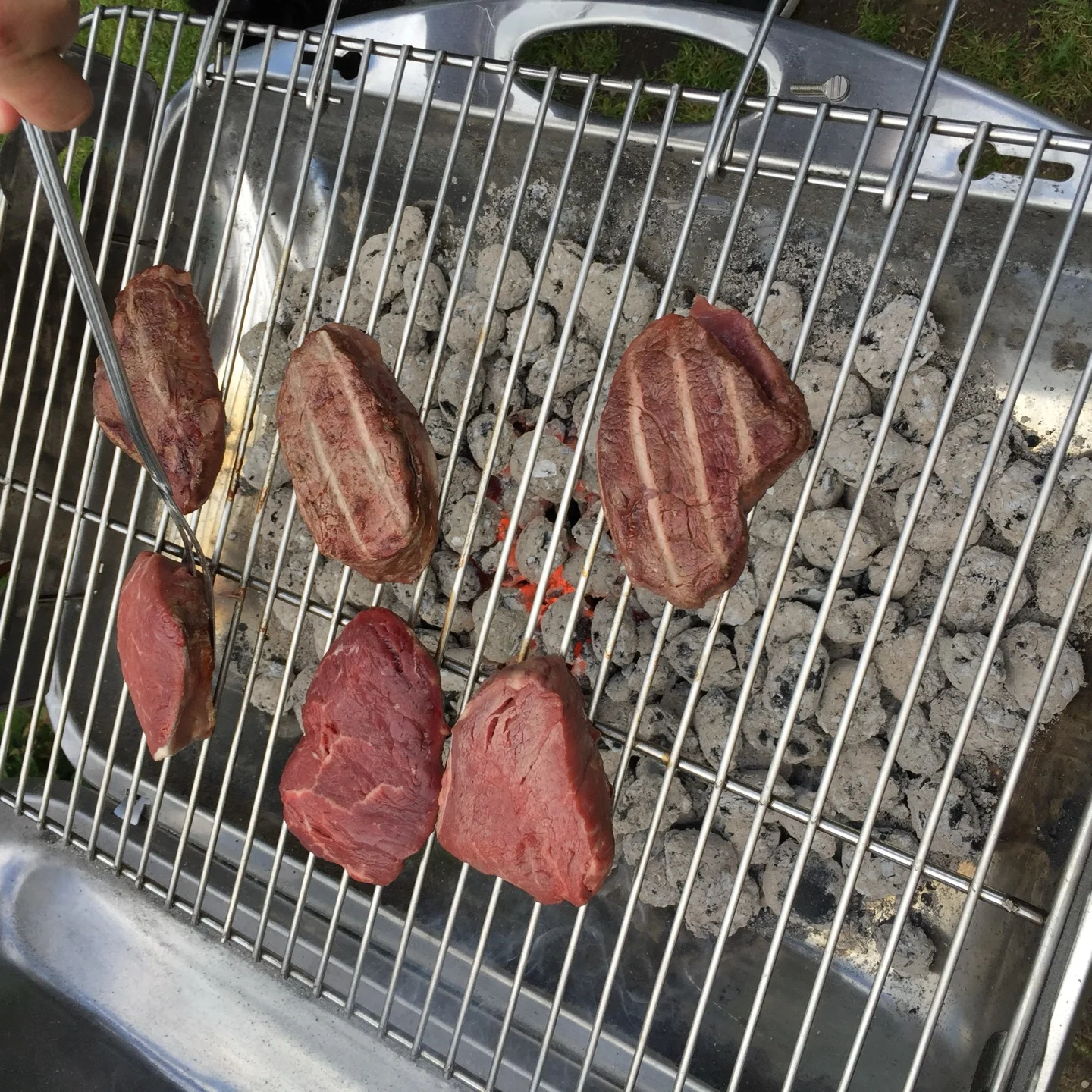 Sechs Steaks auf einem schwarzen Holzkohle-Kugelgrill