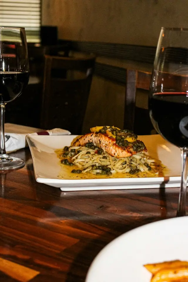 Lachs-Pasta-Gericht im Restaurant-Setting mit Rotweingläsern