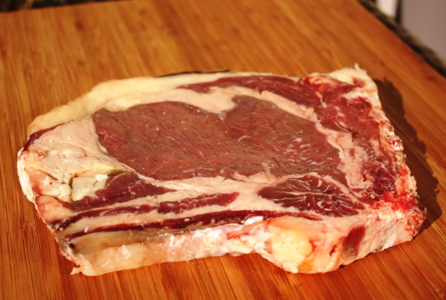 Rohes Dry-Aged Rib-Eye mit sichtbarer Reifungskruste auf Holzbrett