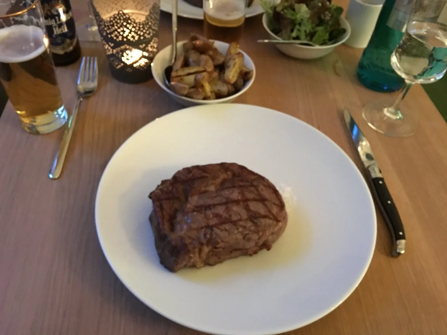 Steak mit Grillstreifen auf weißem Teller im Restaurant, mit Bier und Kartoffeln